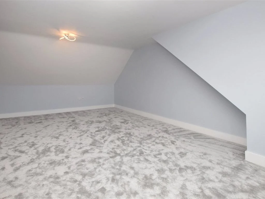 Empty attic room with sloped ceiling, light gray walls, and beige carpet.