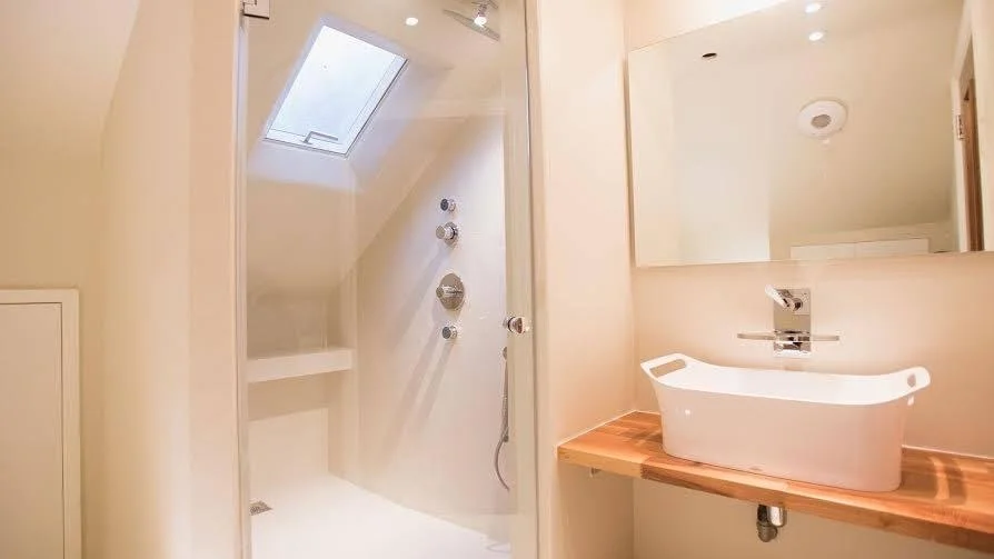 Modern bathroom with a walk-in shower, skylight, and a white vessel sink on a wooden countertop.