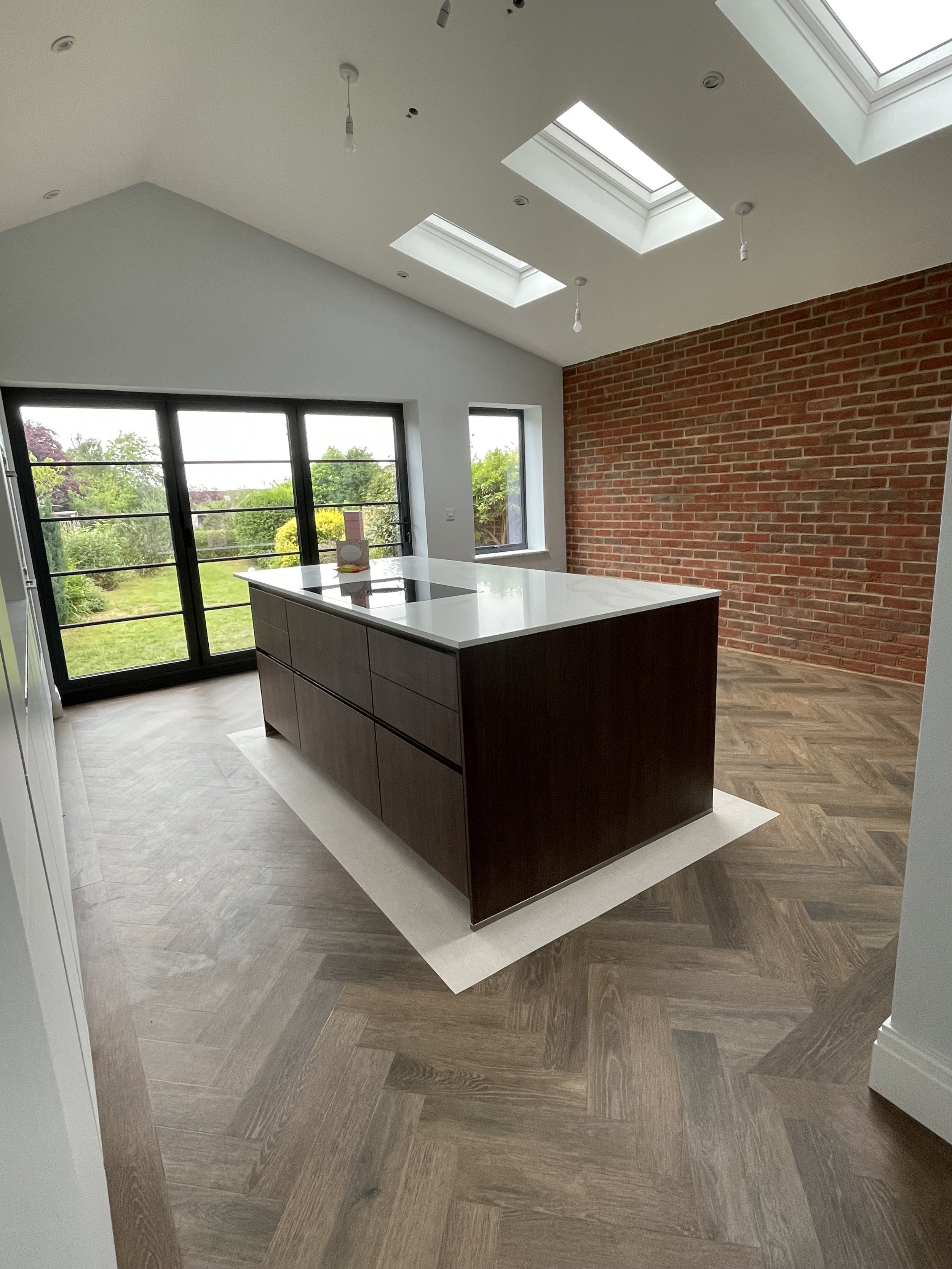 Modern kitchen with a central island, brick accent wall, skylights in the ceiling, large glass doors, and hardwood flooring.