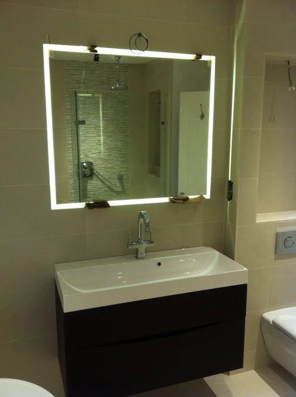 Modern bathroom with a glowing mirror, a white sink with a black cabinet, and a toilet.