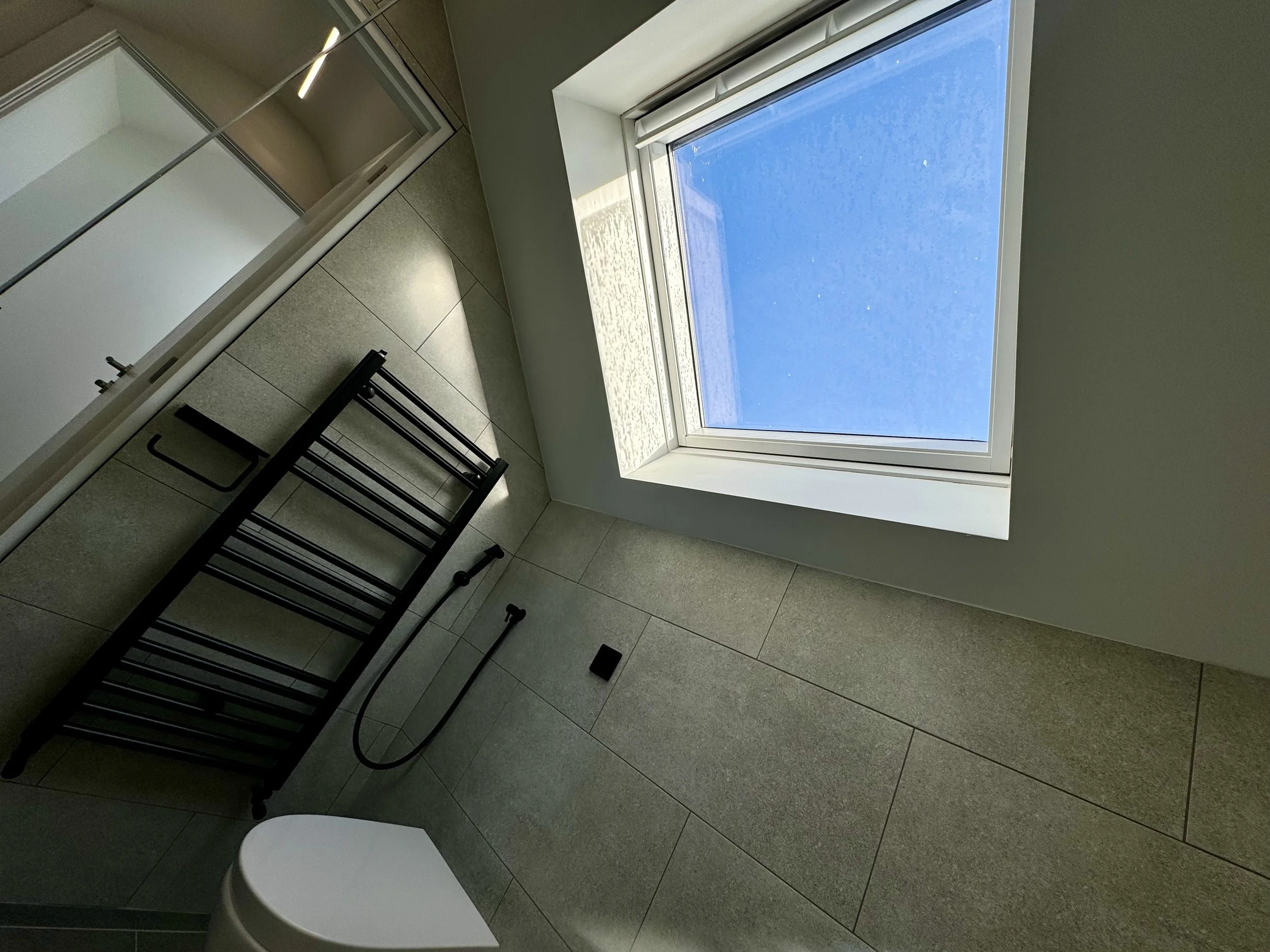 Modern bathroom with a large window showing a clear blue sky, a black towel rack, and a bidet.