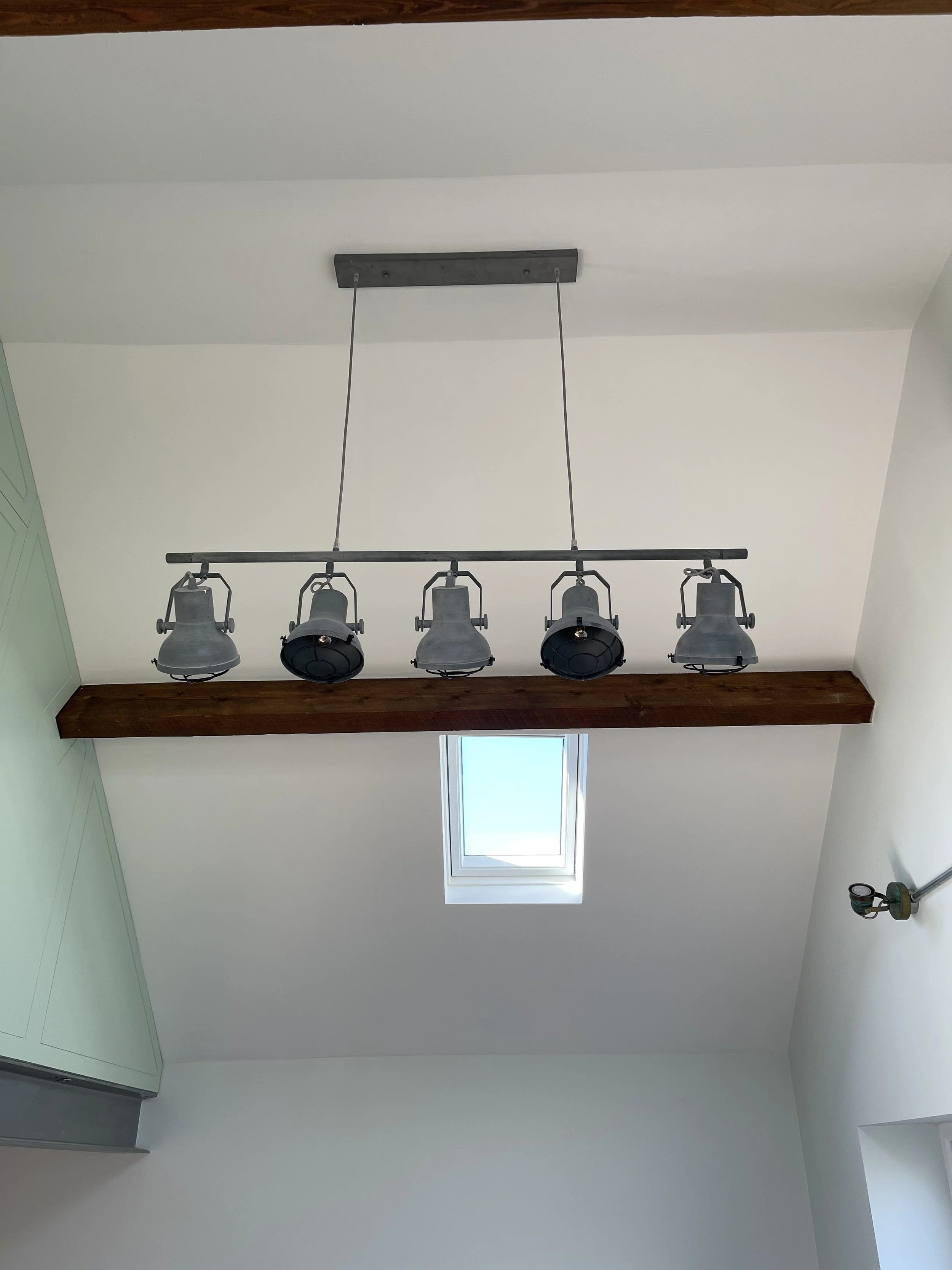 Overhead view of a ceiling with a rustic chandelier light fixture hanging above a skylight window and part of a green kitchen cabinet.