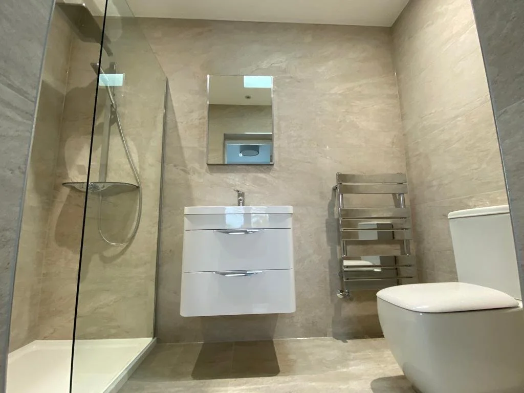 Modern bathroom featuring a walk-in shower with a glass door, a small white vanity with a sink, a wall-mounted mirror, a silver towel rack, and a white toilet.