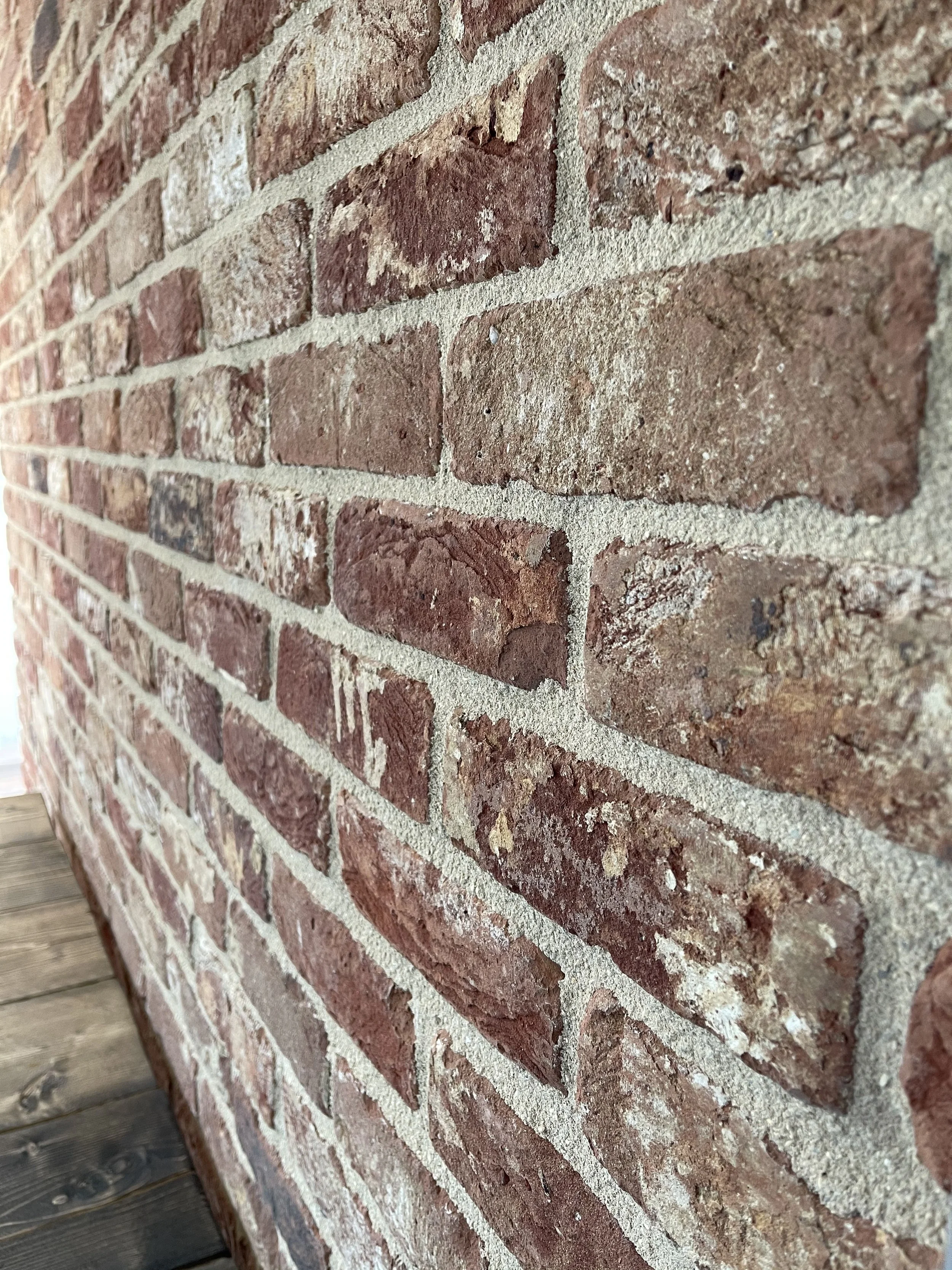 Close-up of a red brick wall with beige mortar, showing a textured and weathered surface.