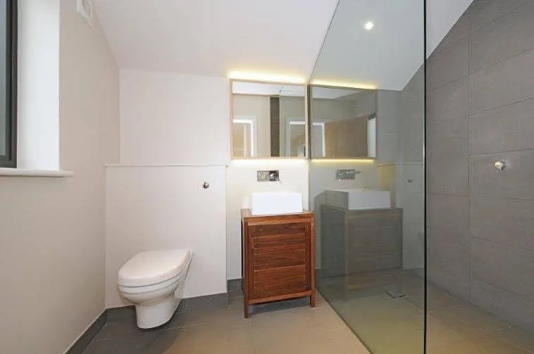 Modern bathroom with white wall, toilet, wooden vanity with vessel sink, large mirror, and glass shower enclosure.