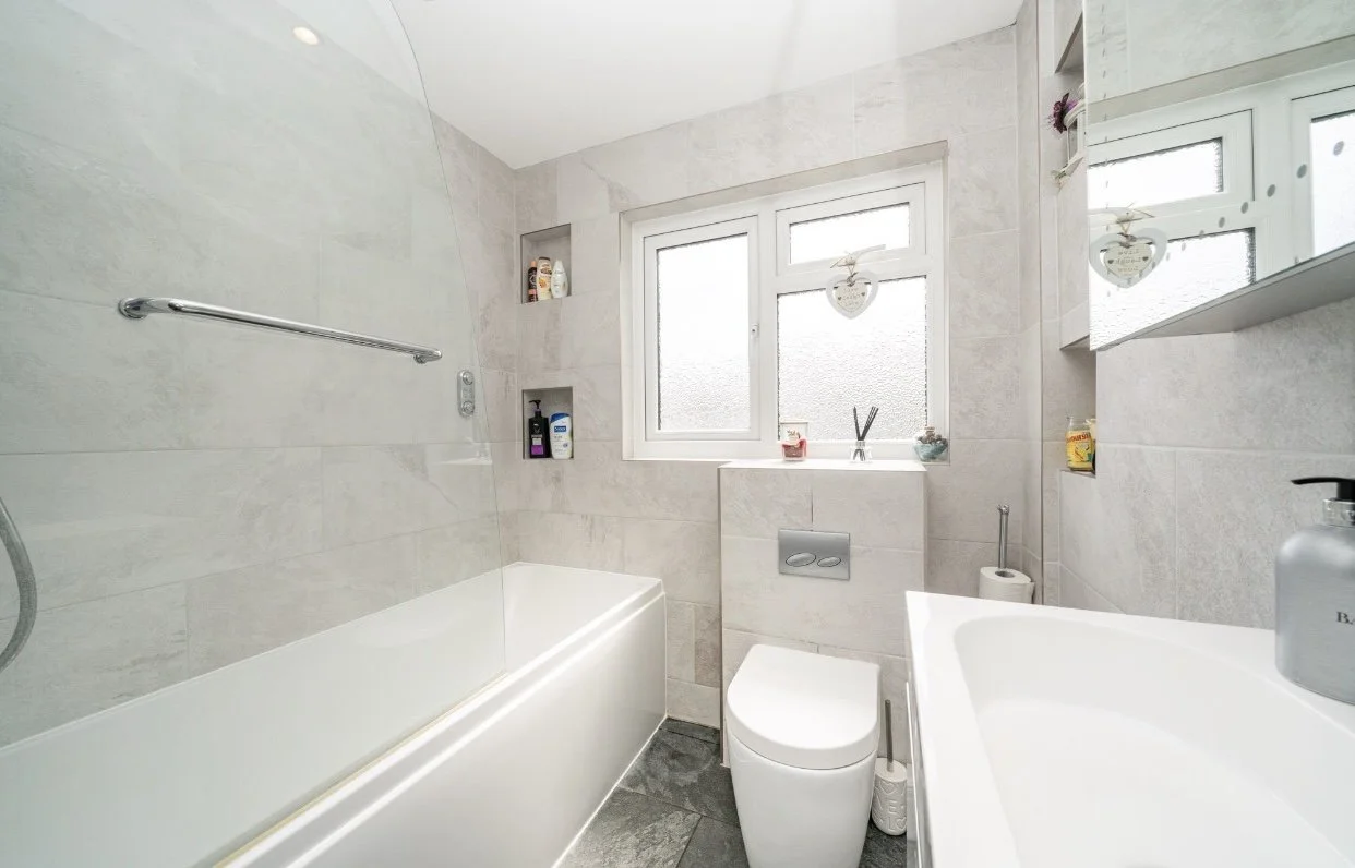 Small modern bathroom with a bathtub, toilet, and sink, featuring frosted windows and decorative heart-shaped ornaments.