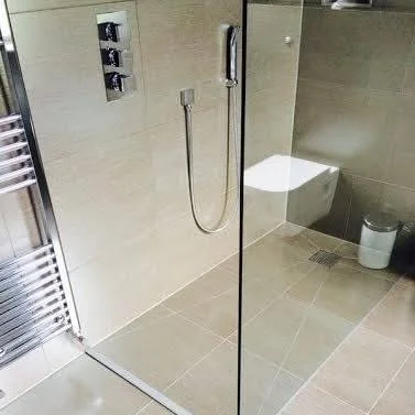 Modern walk-in shower with beige tiled walls and floor, handheld showerhead, and partial view of toilet.