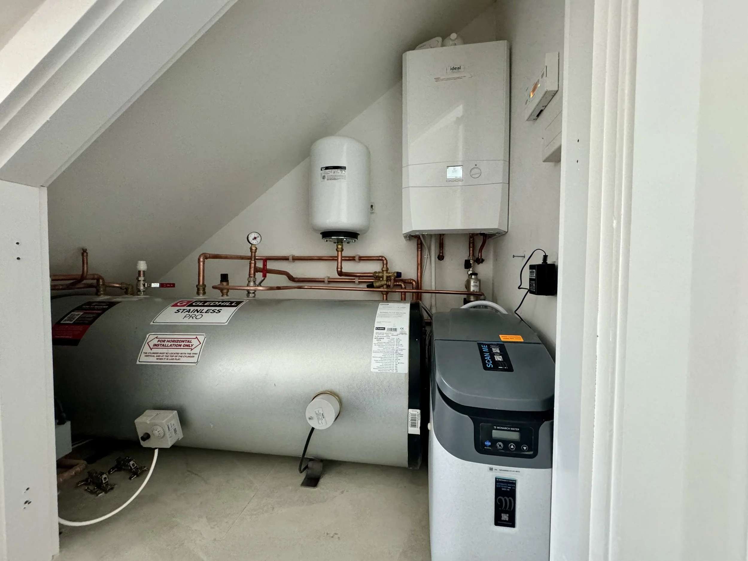 Water heater and boiler system with pipes, gauges, and control units in a small utility closet.