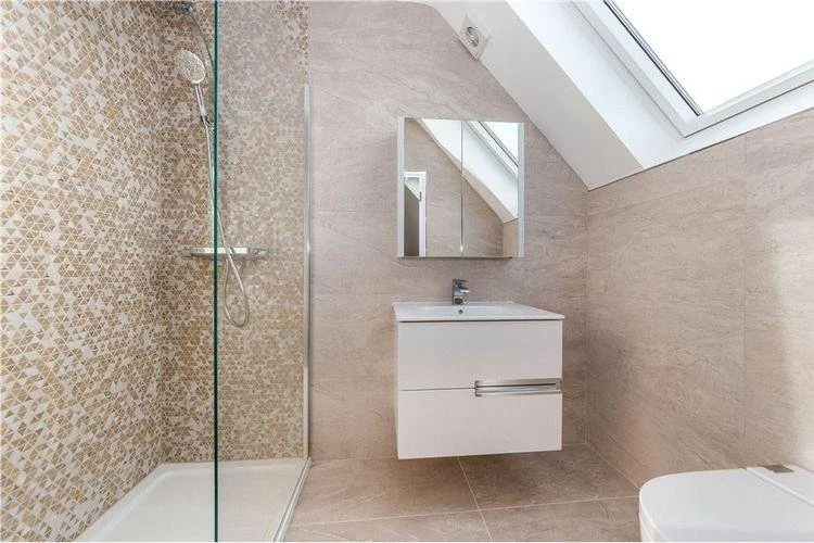 Modern bathroom with a walk-in shower, a wall-mounted sink with a mirror above, and a sloped ceiling with a skylight window.