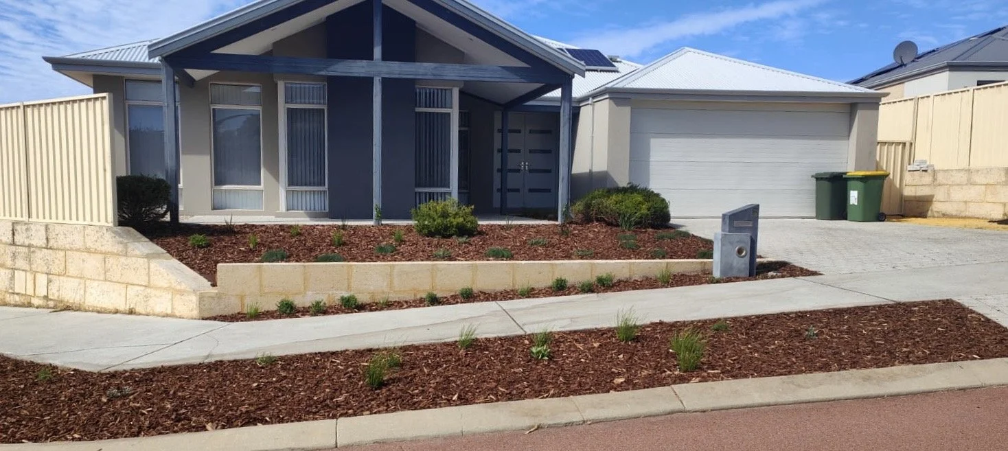 Front view of a modern house with a landscaped yard, small bushes, and a two-car garage, with a sidewalk and driveway in front.