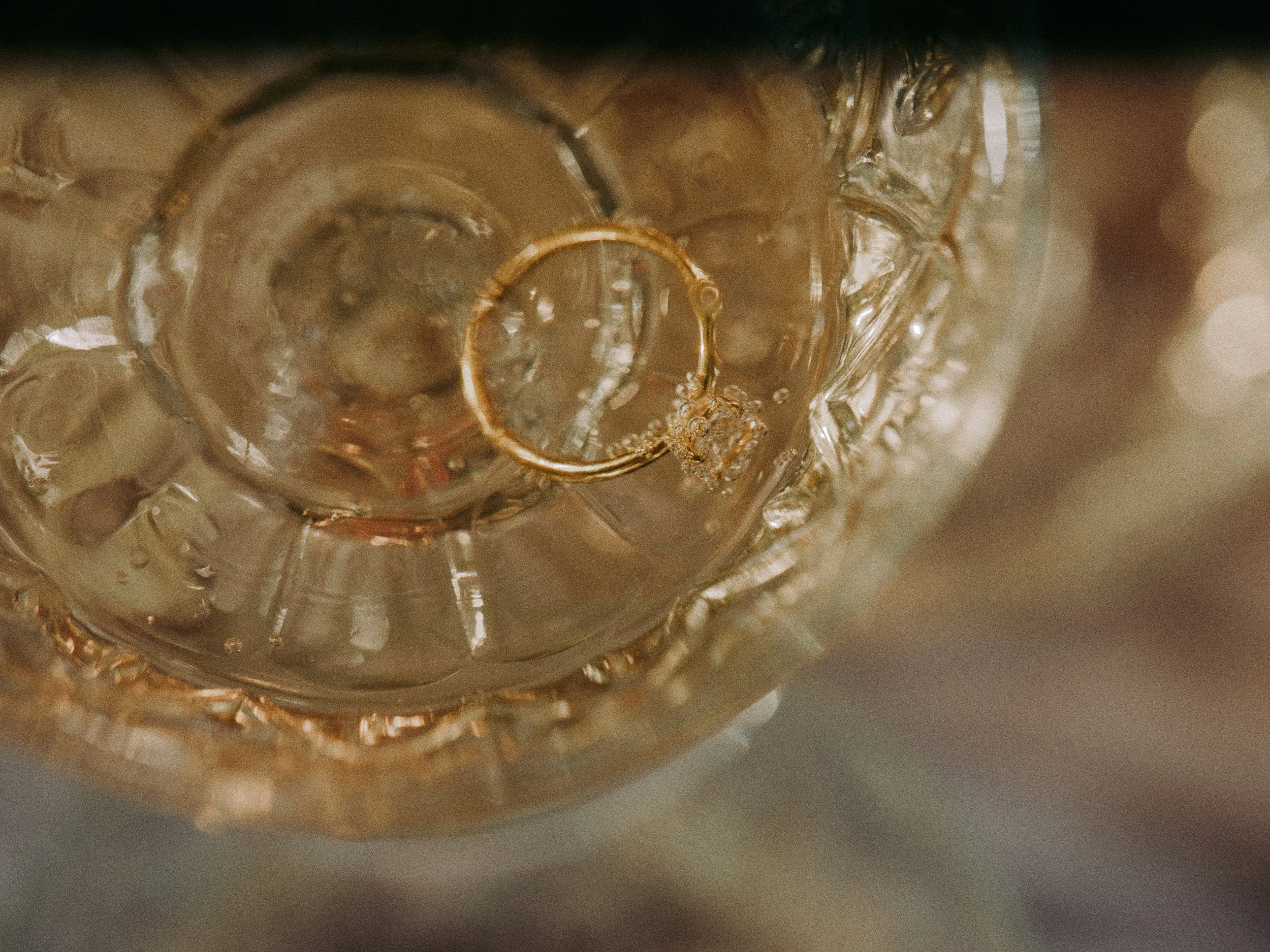 Top-down view of a glass with a gold ring and a diamond ring inside, with ice cubes and sparkling bubbles.