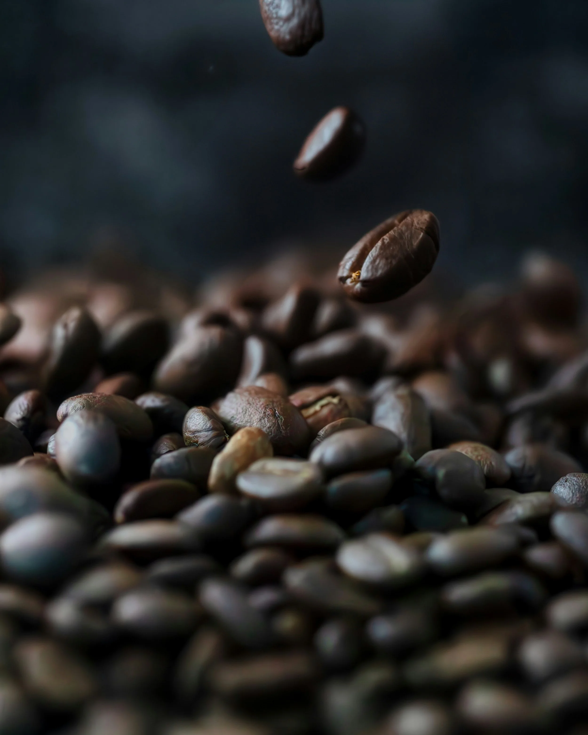 Close-up of coffee beans, some falling through the air onto a pile.