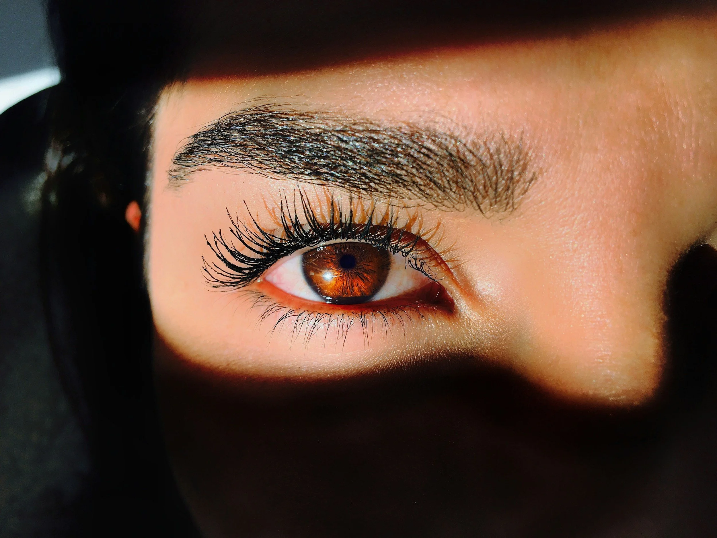 Close-up of a person's face, focusing on one eye with detailed brown iris and long eyelashes, with well-defined eyebrow and skin texture.