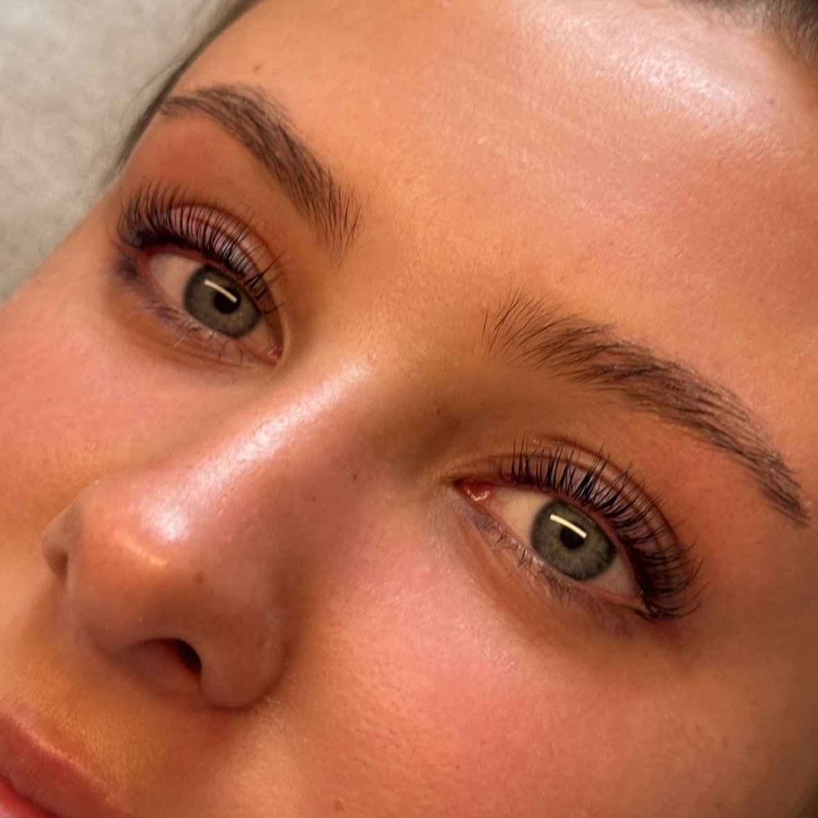 Close-up of a woman's face showing her eyes, eyebrows, and part of her nose with natural makeup and long eyelashes.