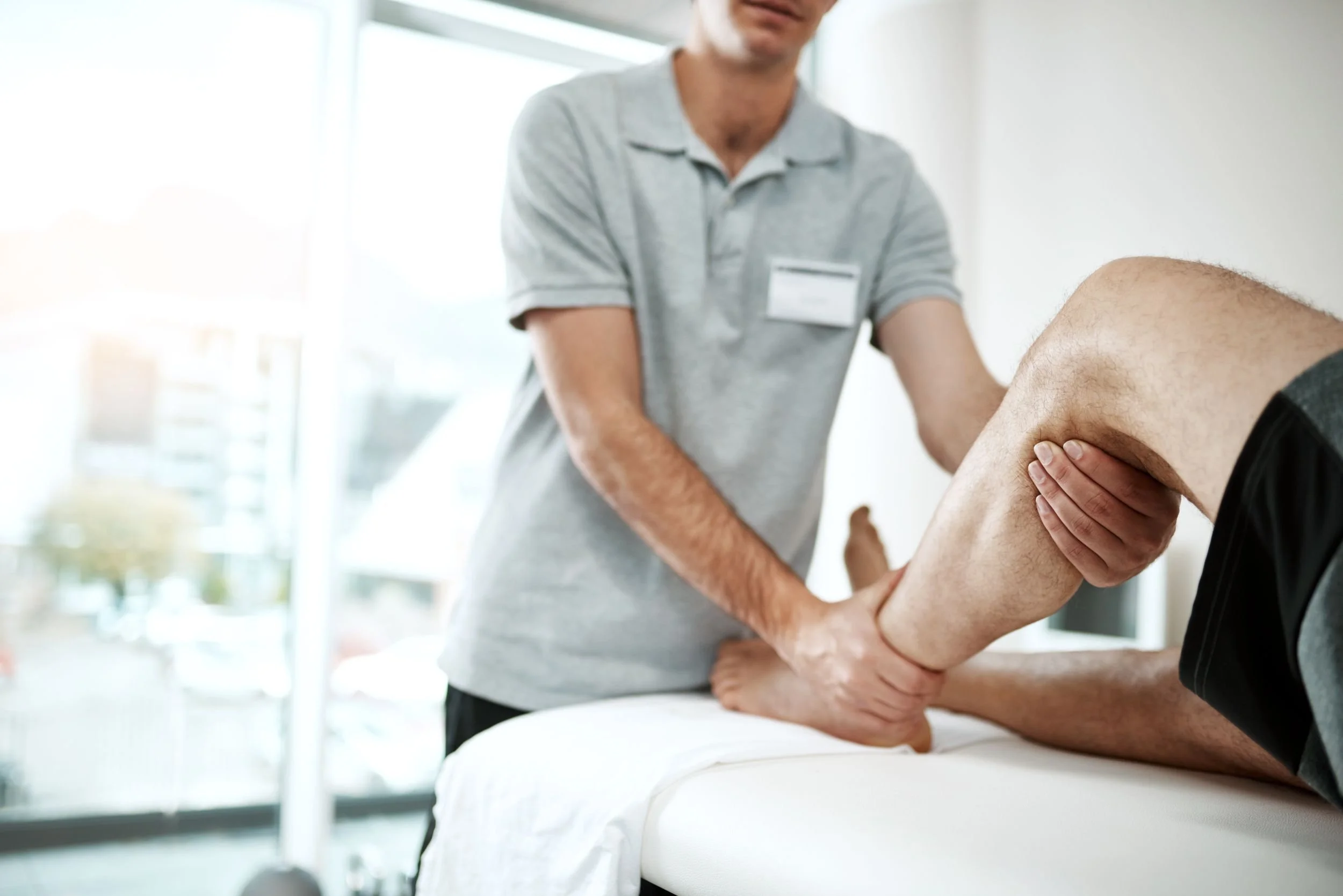 Ein Physiotherapeut behandelt das Knie eines Patienten im Behandlungsraum.