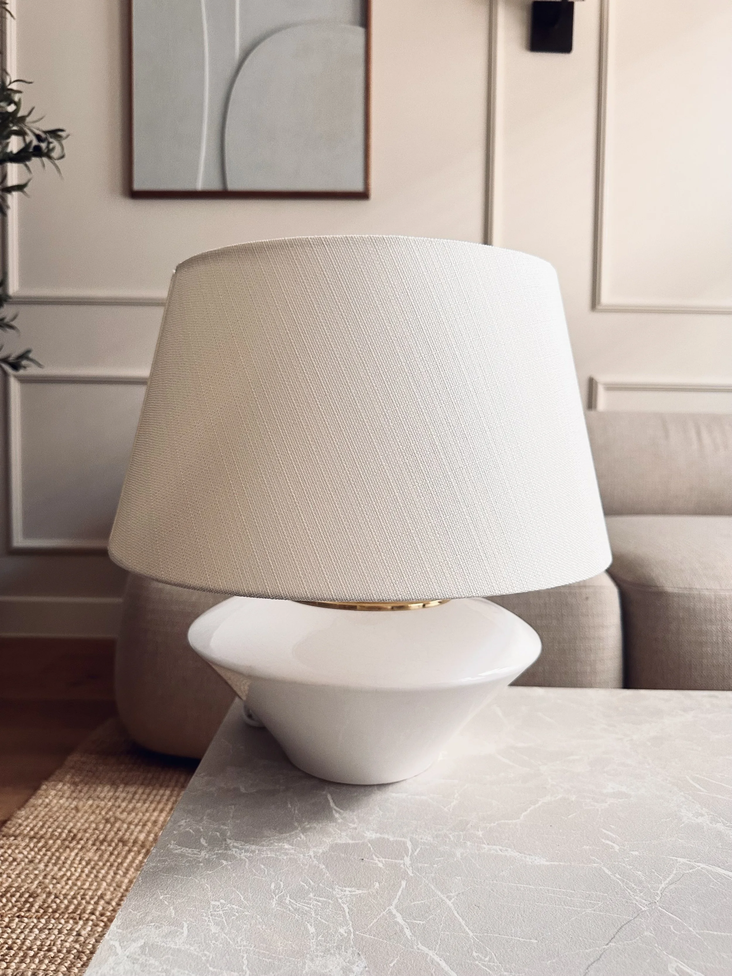 Witte tafelvlam met beige circulaire lamp op een marmeren tafel in een woonkamer met beige bank en muurdecoraties.