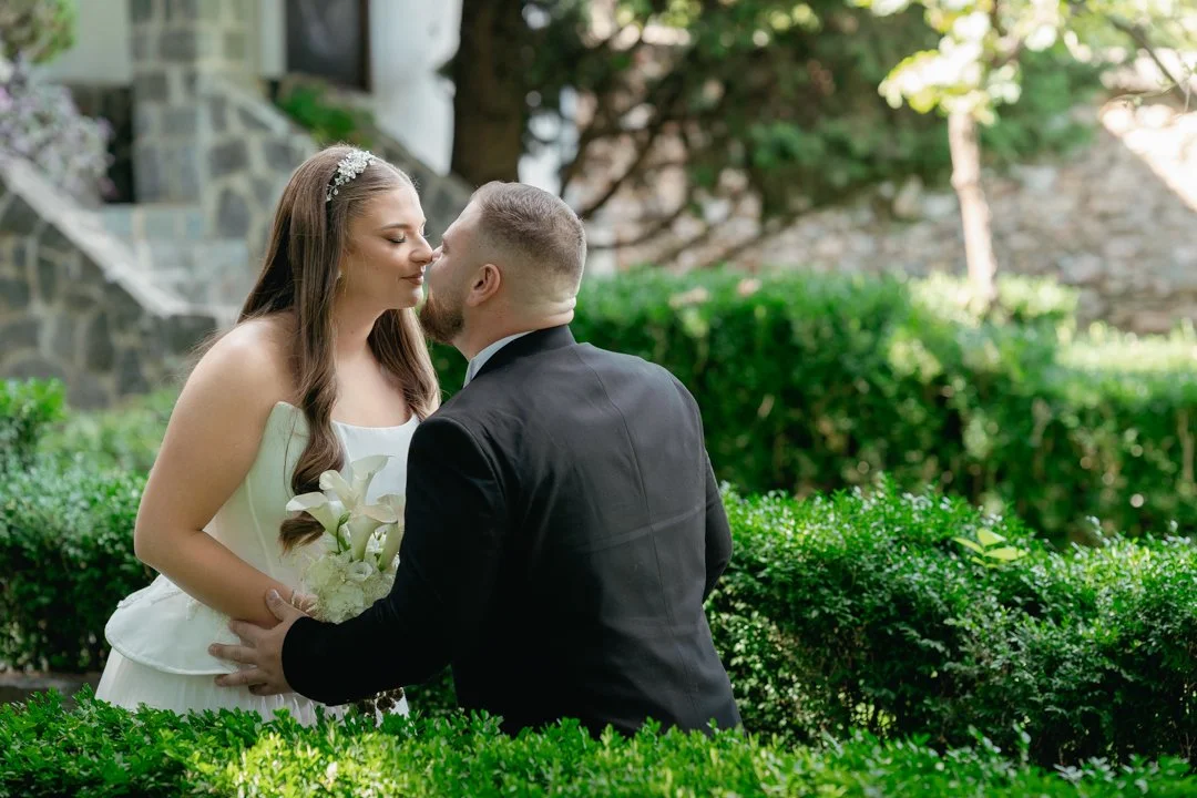 A bride and groom share a kiss in a garden, surrounded by greenery.