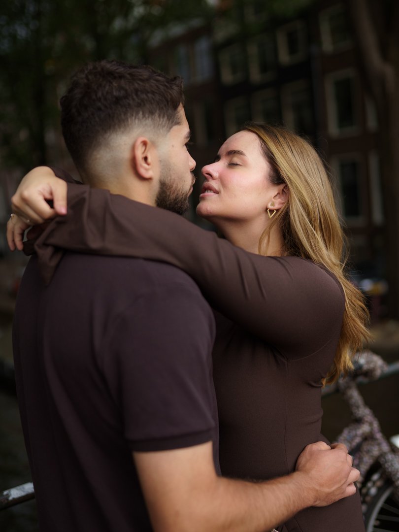 A couple sharing an intimate moment, embracing closely and about to kiss outdoors near a canal or river.