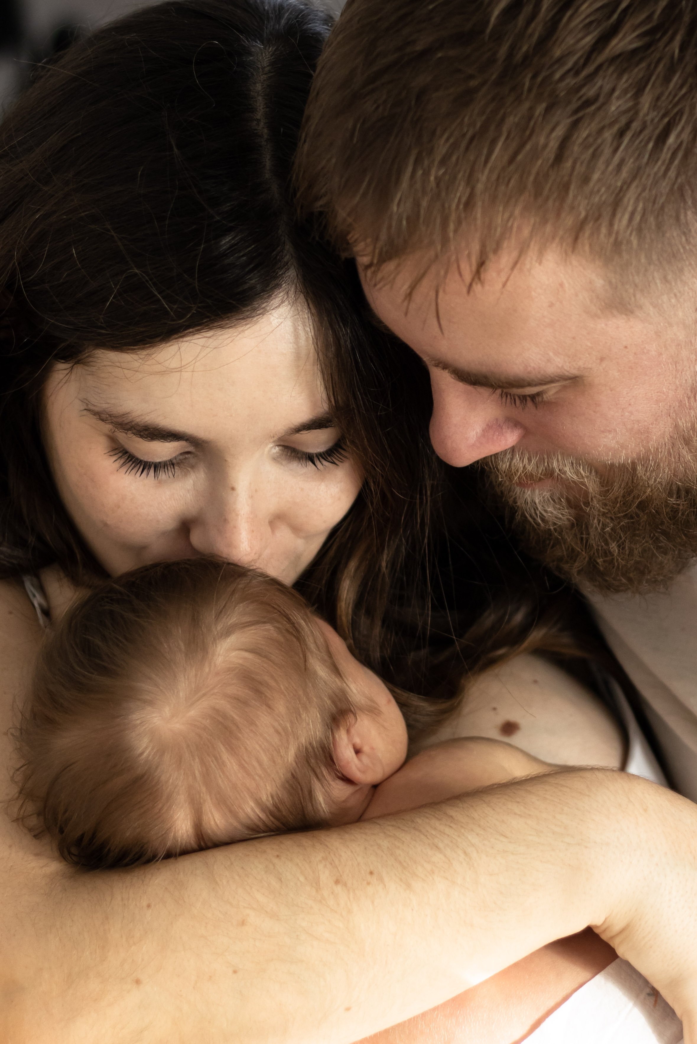 Une femme, un homme et un bébé se retrouvent dans une étreinte intime et affectueuse.
