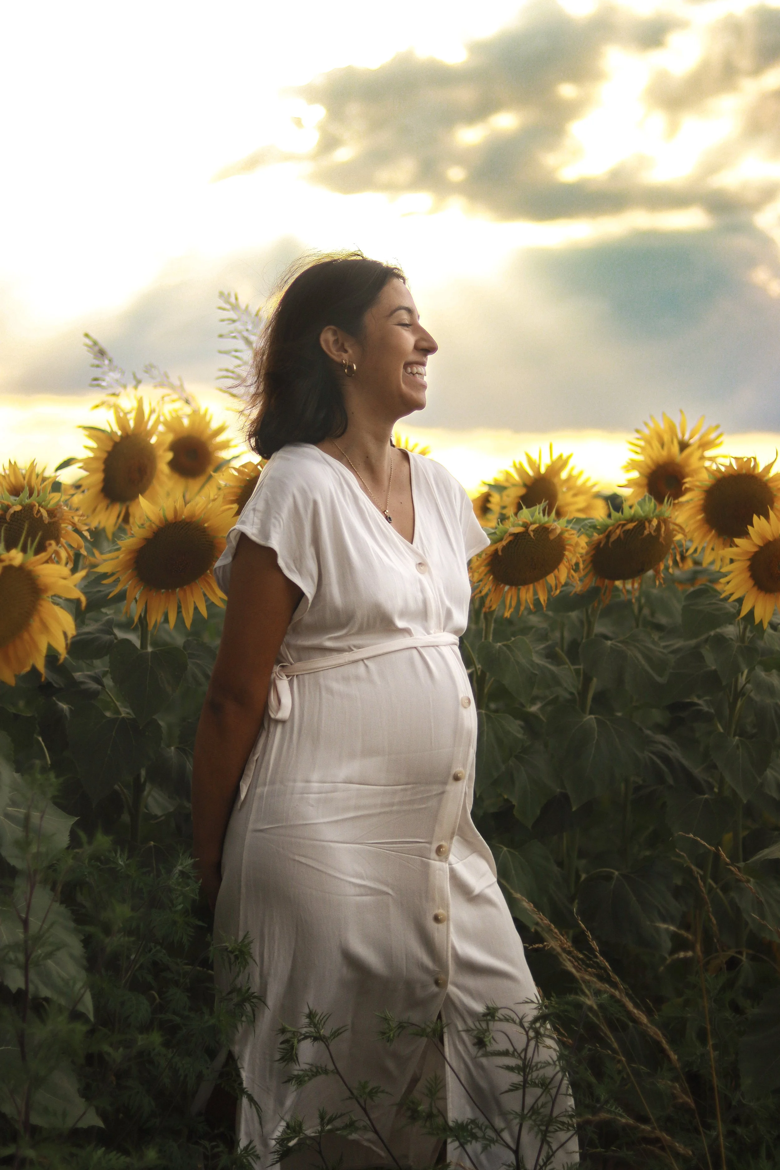 Une femme enceinte souriante dans un champ de tournesols au coucher du soleil.
