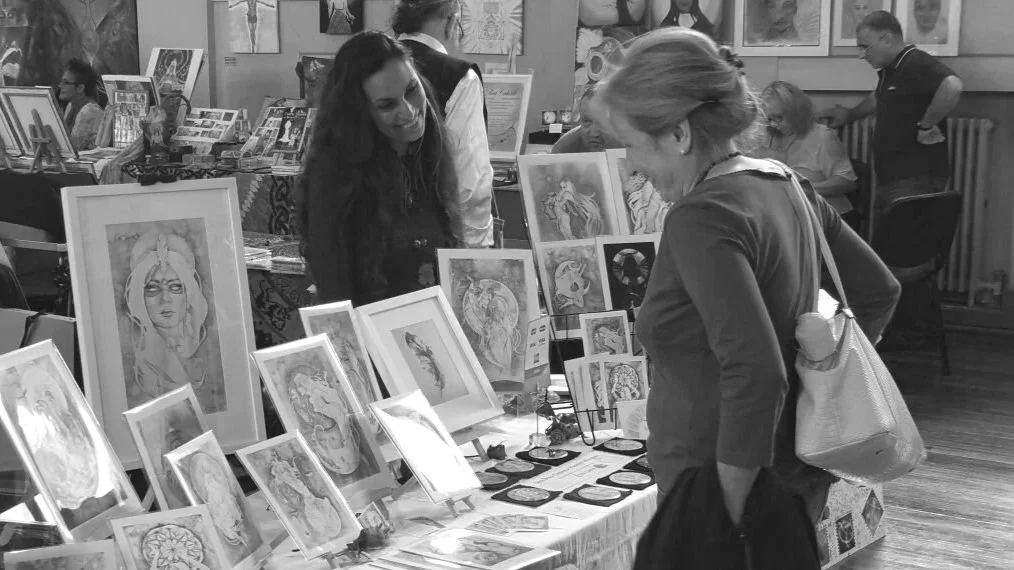 Woman browsing framed artwork and prints at a crowded indoor art fair booth