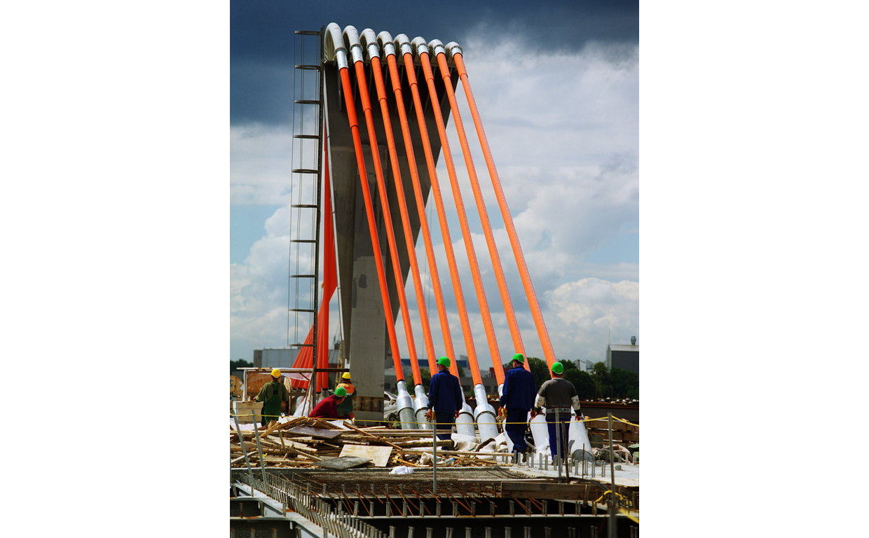 Construction workers in safety gear working on a bridge under a partly cloudy sky.