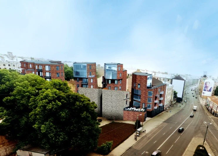 Modern multi-story brick buildings with glass upper floors near a busy road, trees, and billboards.