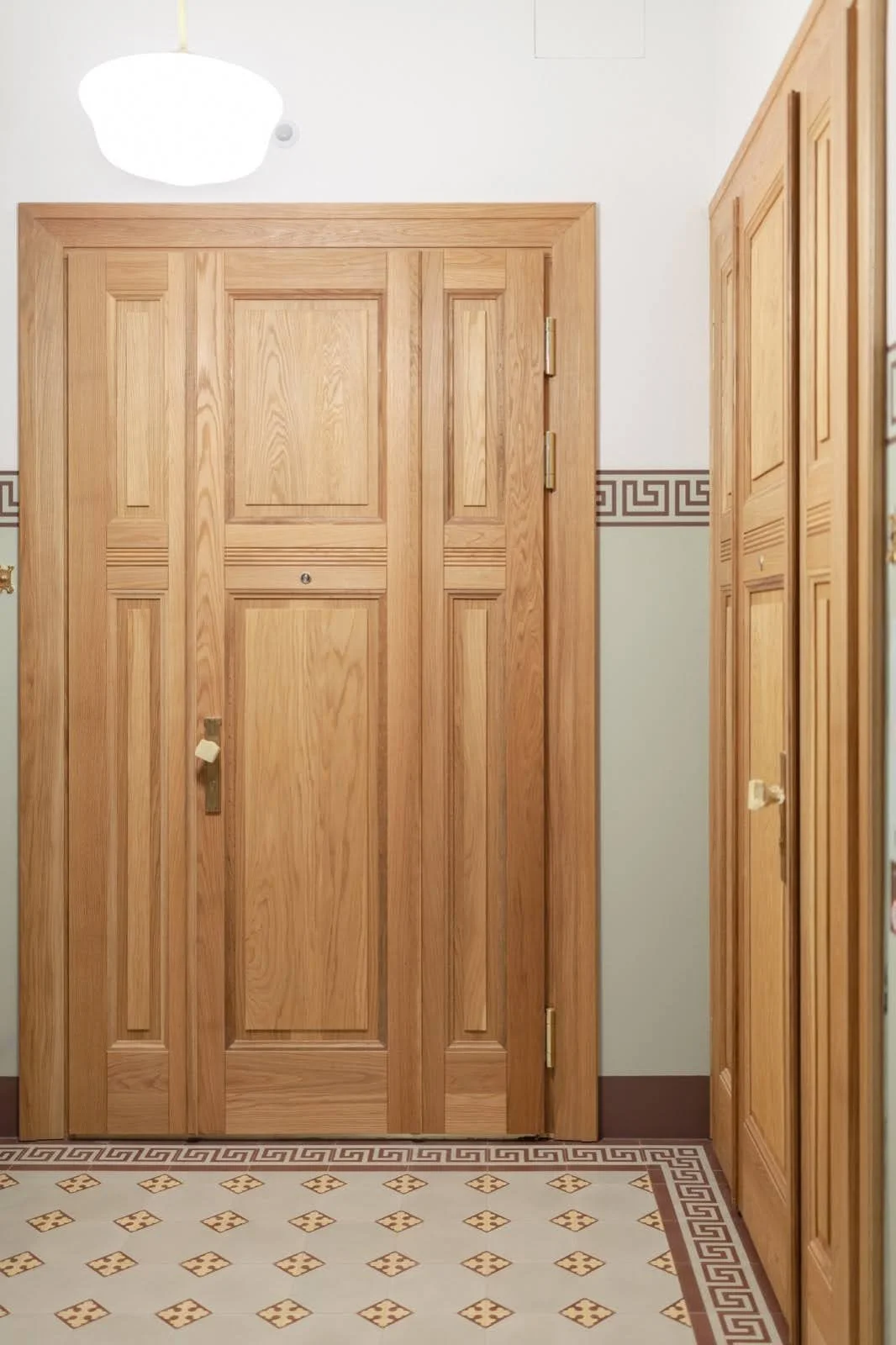 Wooden door with a peephole, and wooden cabinets on the right side in an interior space with patterned tile flooring.