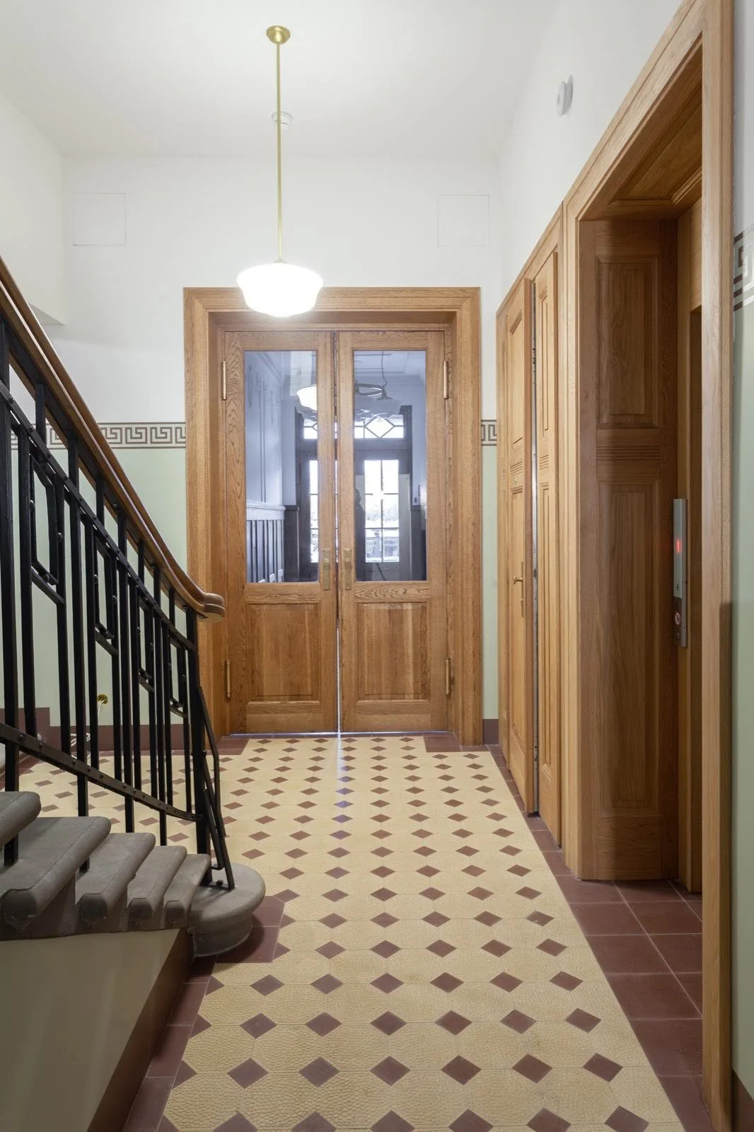 Entryway with wooden double doors, decorative tile floor, and wooden panel walls, featuring an elevator door on the right.