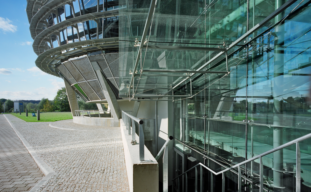 Modern building with glass walls and outdoor walkway, with a curved architectural design and metal railings.