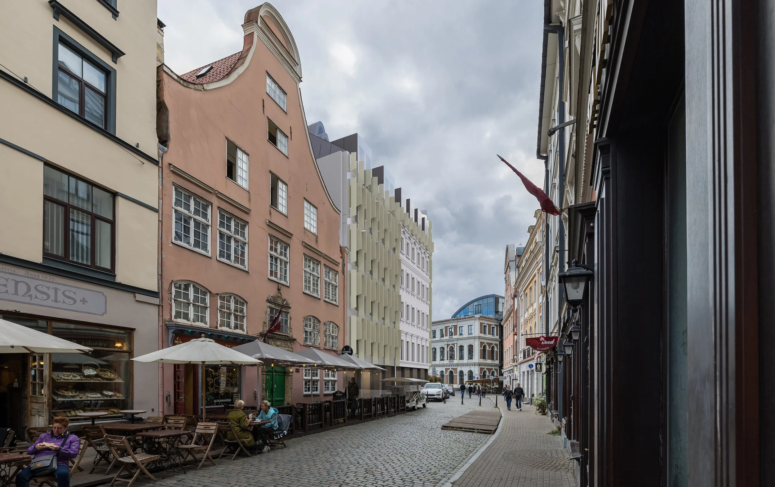 A cobblestone street with outdoor seating, umbrellas, and buildings with diverse architectural styles under cloudy sky.