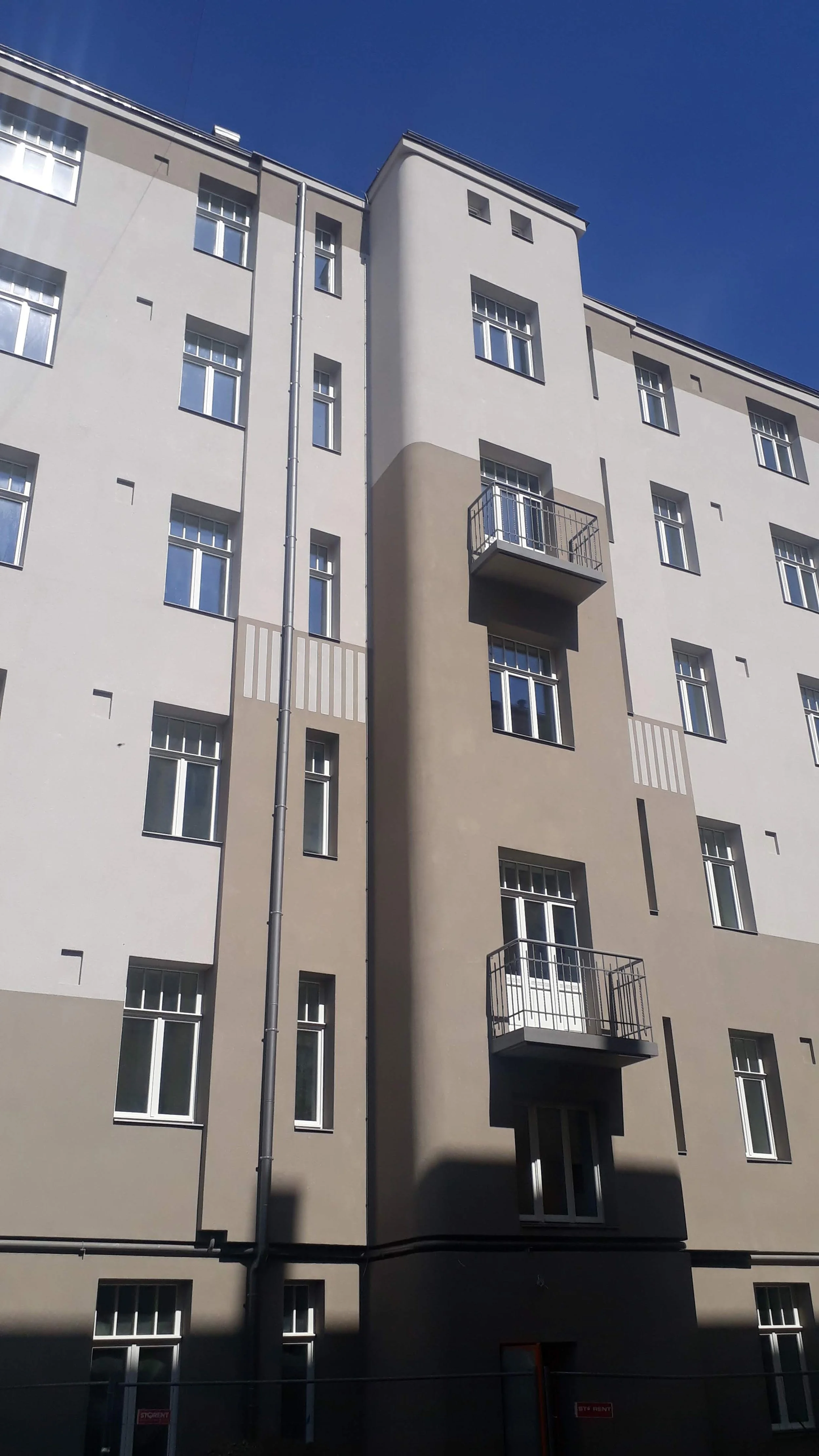 Tall modern apartment building with multiple windows and small balconies, under a clear blue sky.