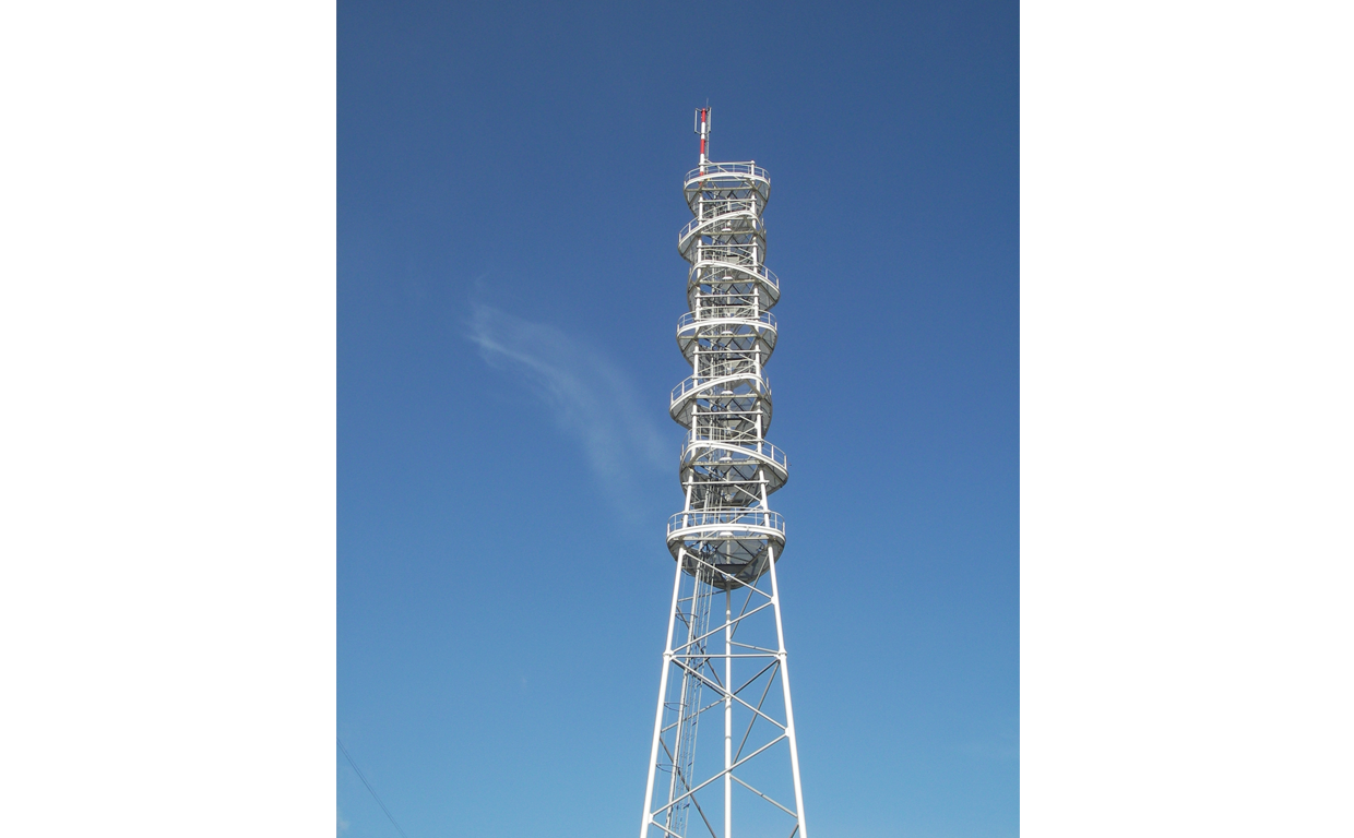 A tall, white radio or communication tower with a spiral staircase around its structure, set against a clear blue sky.