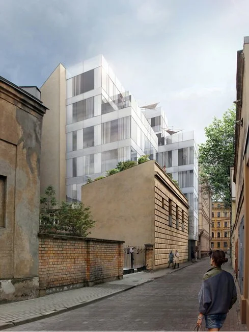 Modern white apartment building with large glass windows and balconies, situated behind older brick and concrete buildings on a city street, with pedestrians walking.