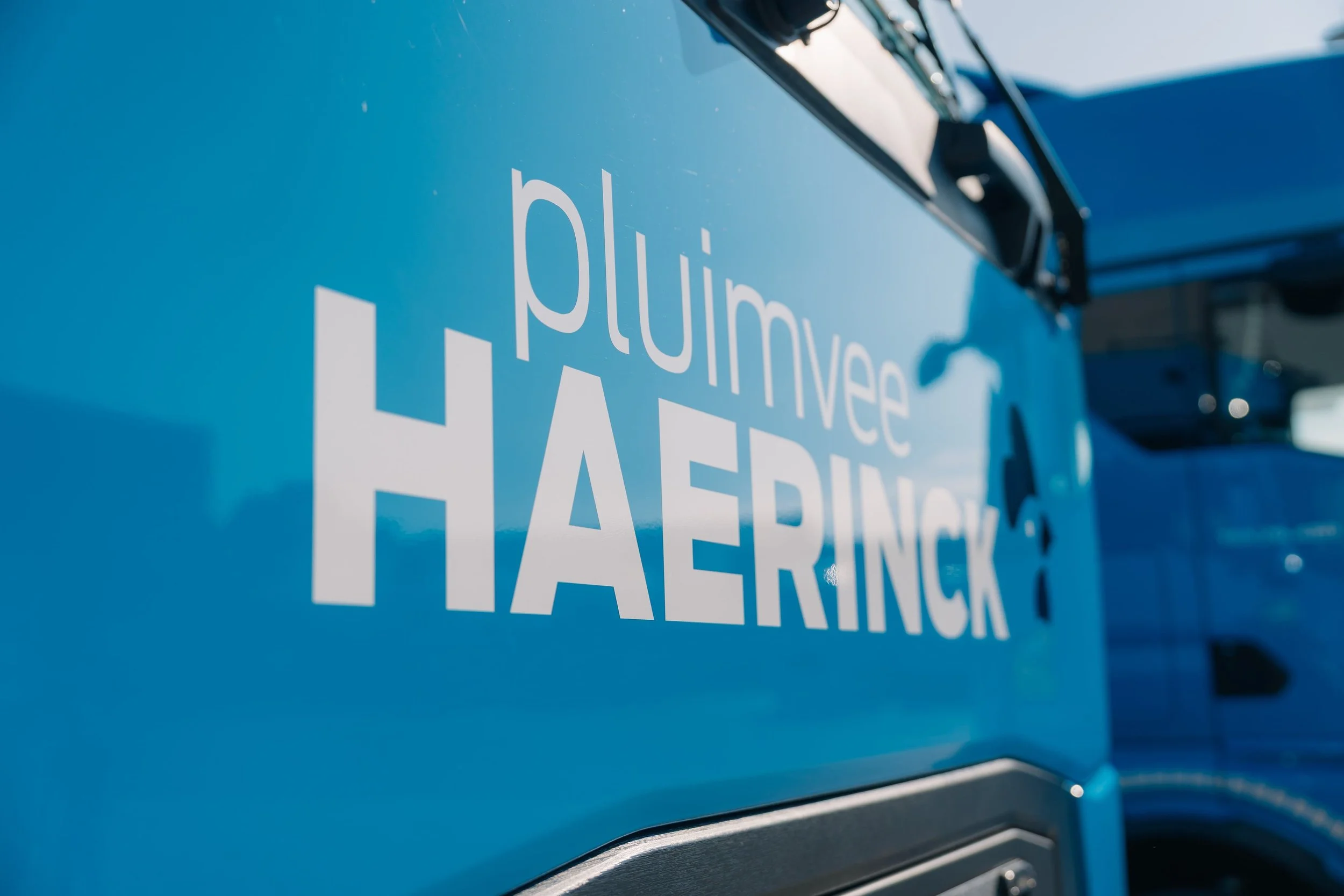 Close-up van een blauwe afvalwagen met witte tekst: 'pluimveem inhaerink'.