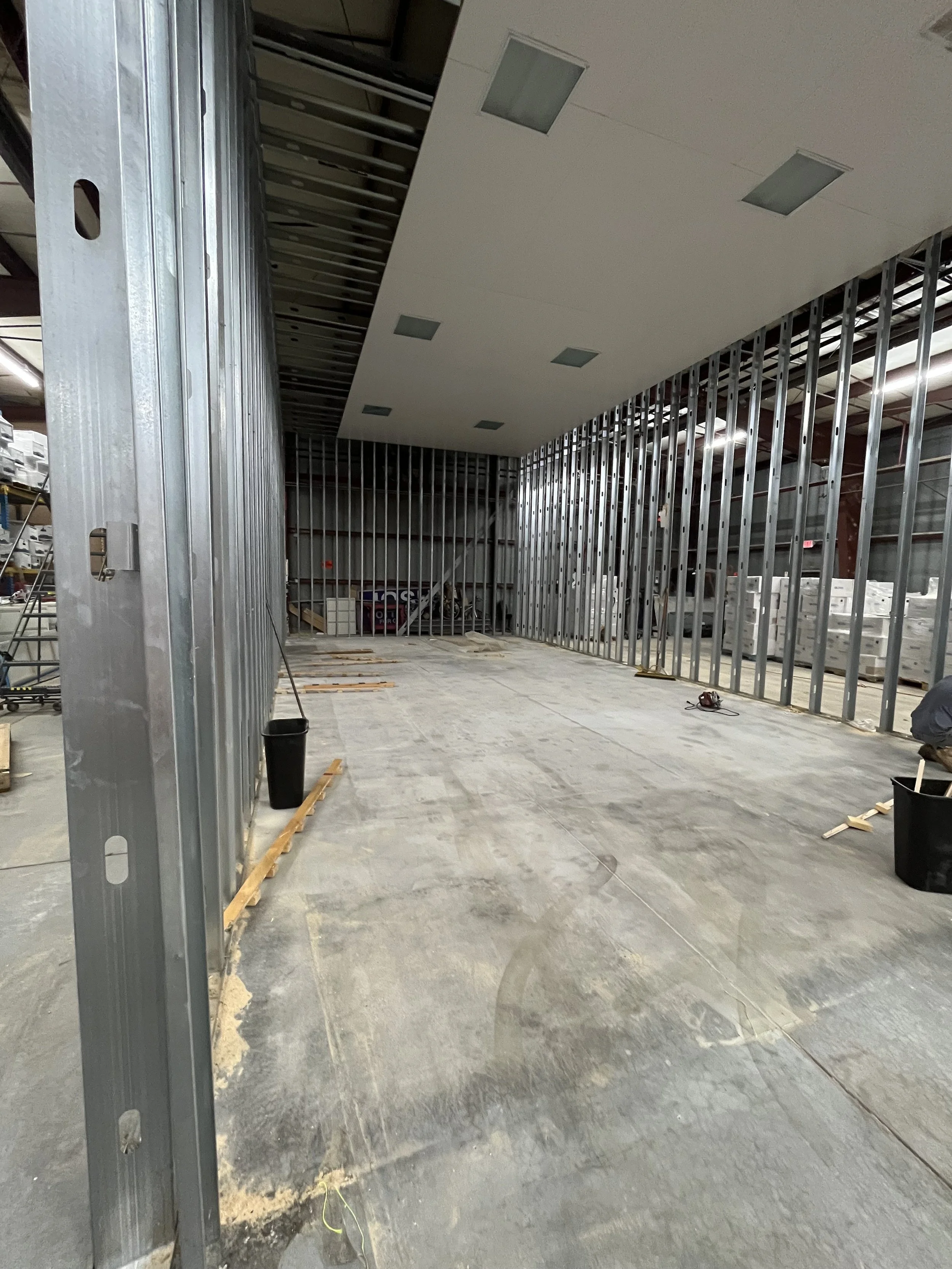 Construction site with metal framing for walls, ceiling panels, and construction tools and materials on the floor.