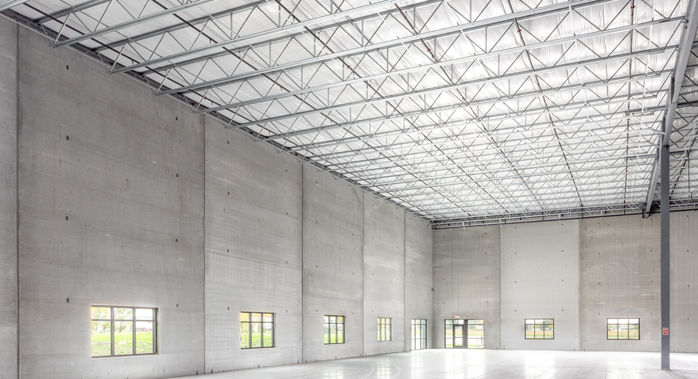 Empty industrial warehouse with high ceiling, concrete walls, and multiple small windows