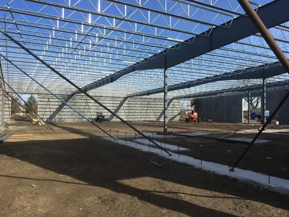 Construction site of a large building with a steel framework and an open ground area, with construction equipment and materials visible.