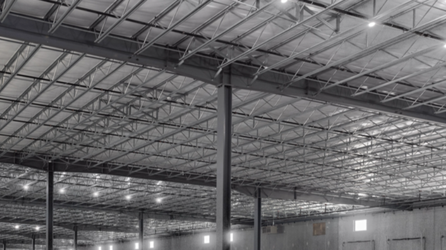 Interior of a large, empty industrial warehouse with metal roof trusses and support columns.