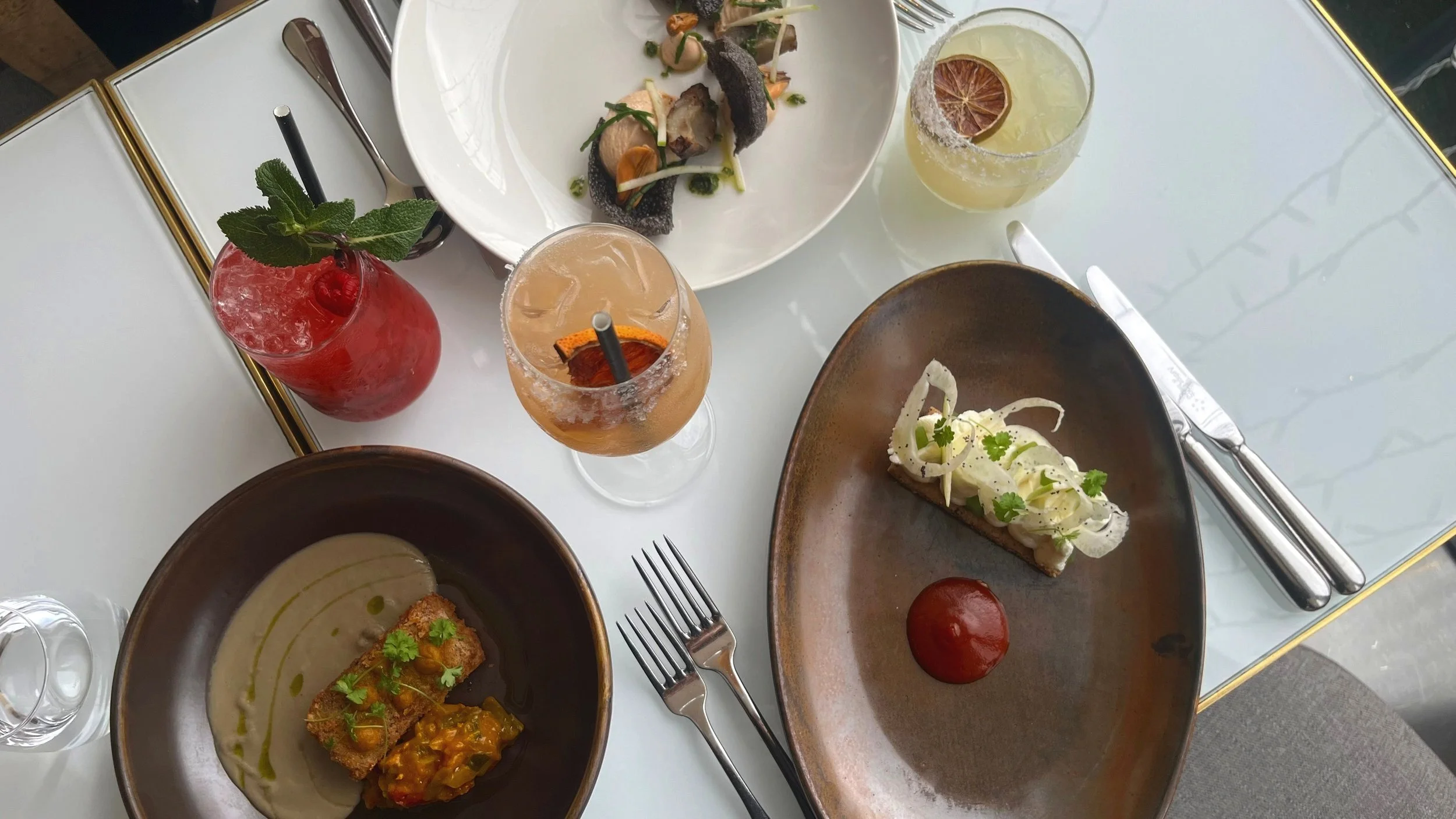 Curated restaurant dining table with multiple gourmet dishes, desserts and cocktails, styled for hospitality social media marketing and luxury food content creation.