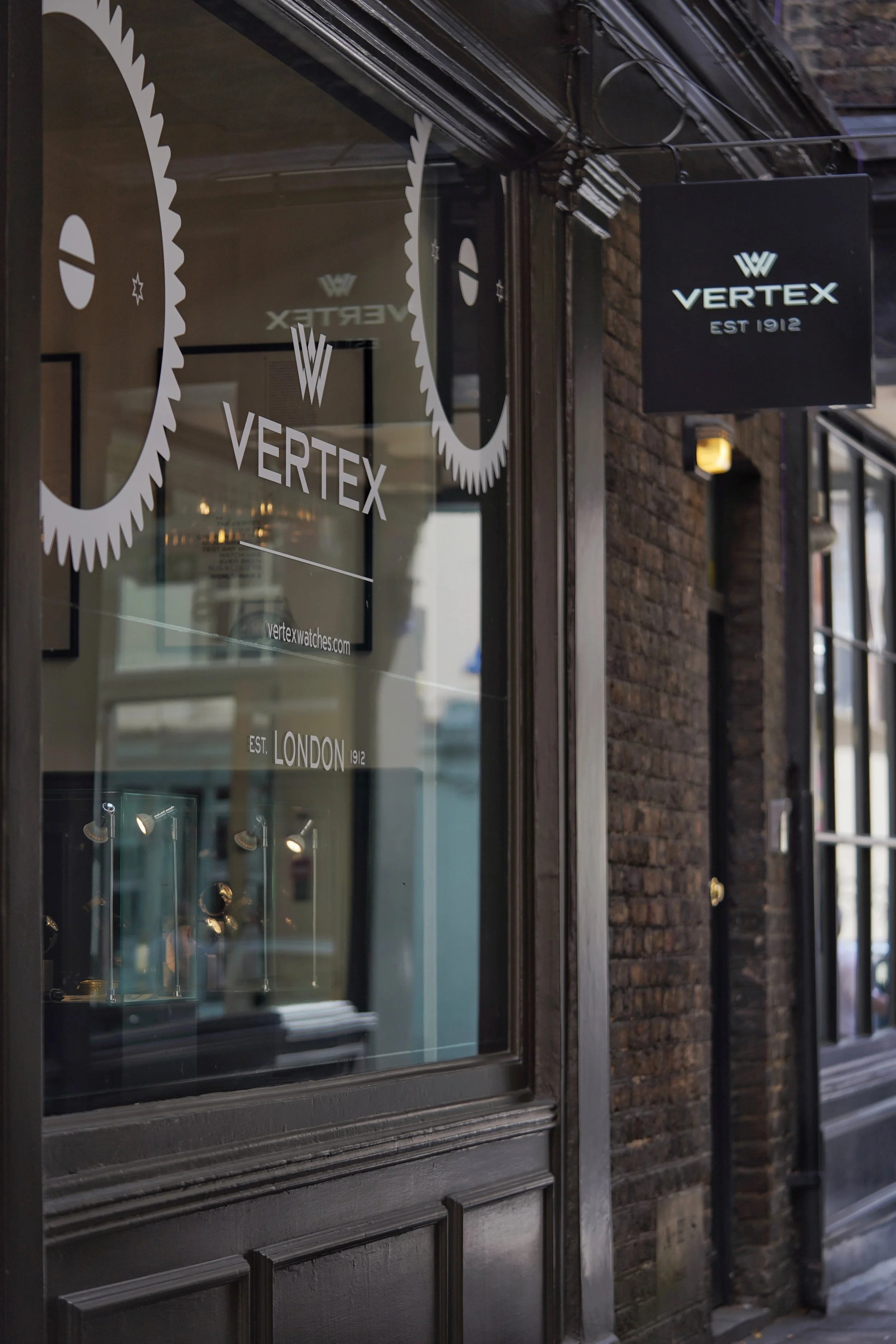Storefront window displaying Vertex Watches logo, with a black sign that reads 'VERTEX EST 1912.'