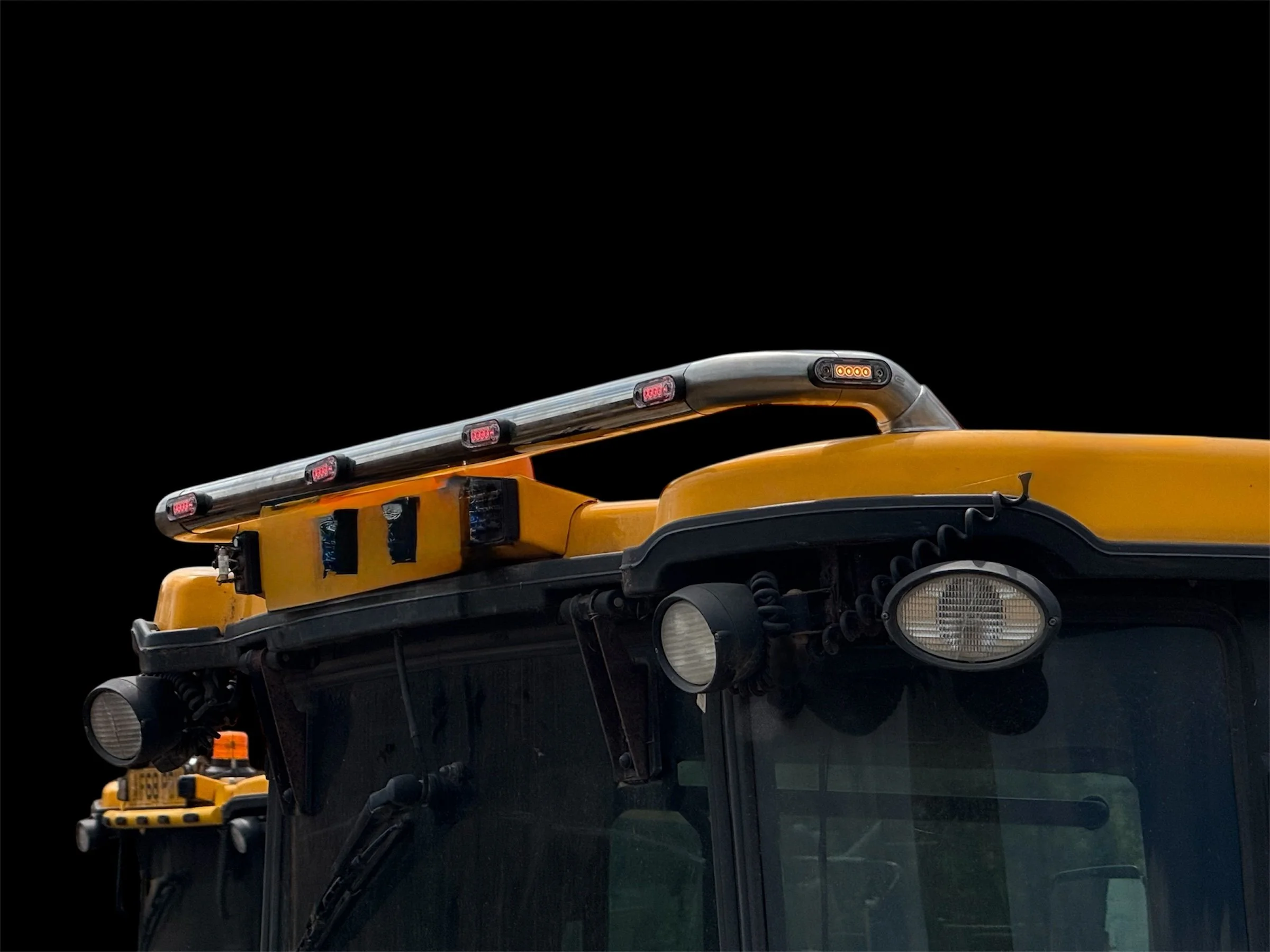 Close-up of a row of yellow school buses with black trim and rounded headlights, viewed from the front, against a plain black background.