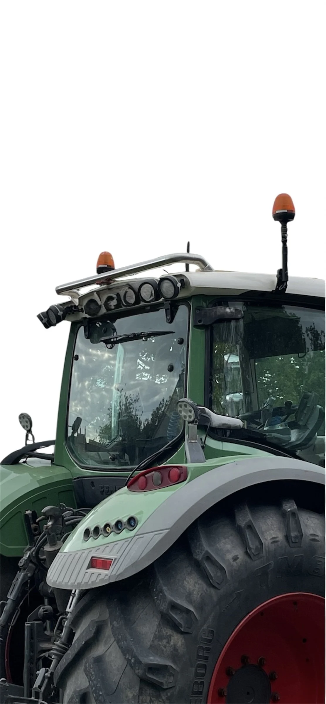 Close-up of a green tractor with an enclosed cabin, large black tires, and orange warning lights on top.