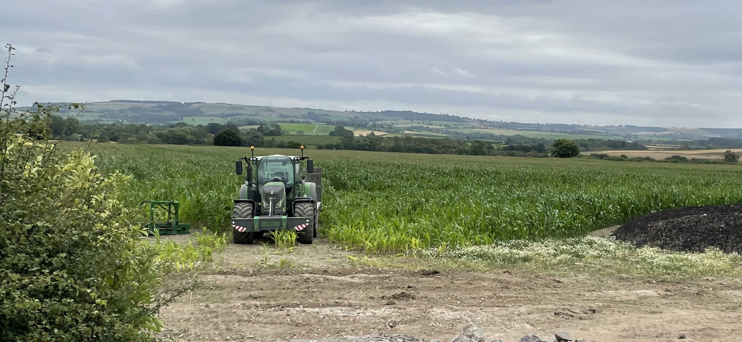 A tractor working in a large green field on a cloudy day, with rolling hills in the background.