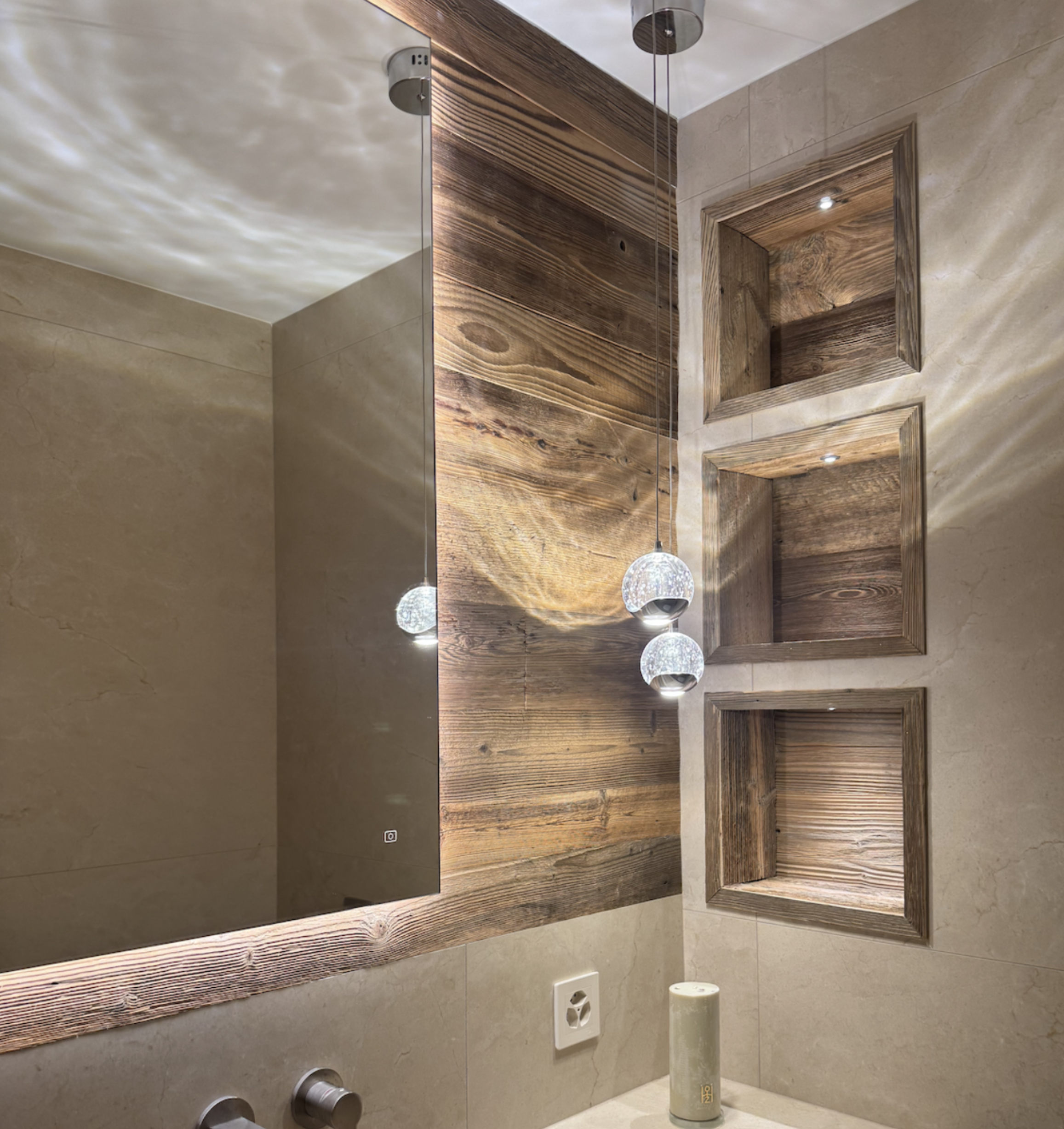 Une salle de bain avec un grand miroir, un mur en bois, des niches encastrées, des lustres suspendus et un décor en nuances de beige et de bois.