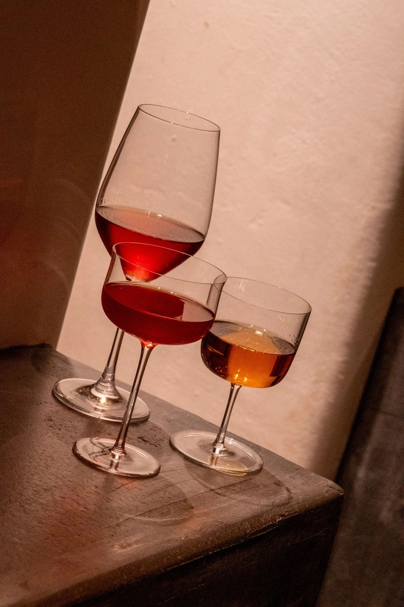 Trois verres à vin avec des vins rouge, rosé et blanc sur une surface en bois.