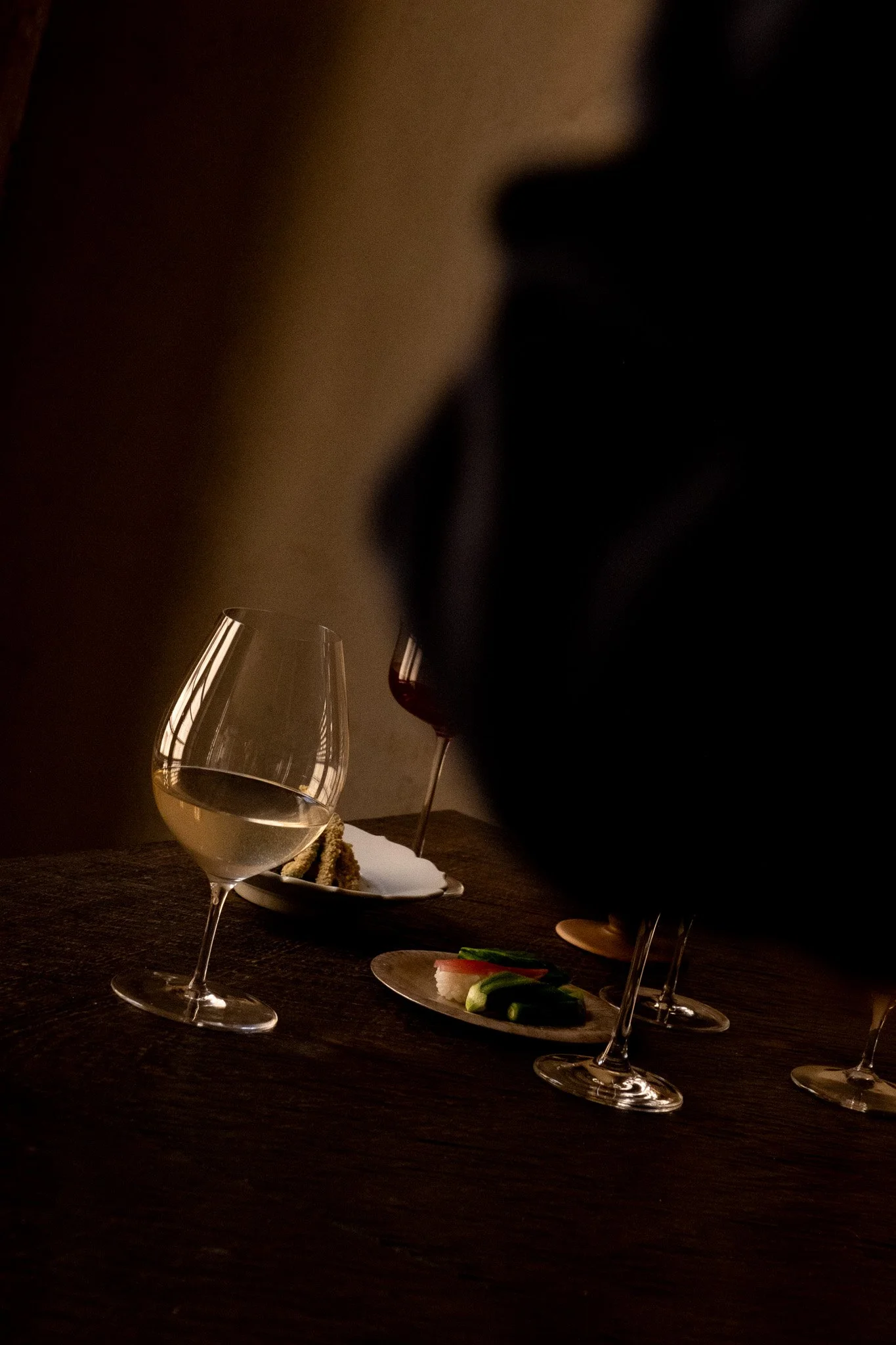 Verre de vin blanc, verre de vin rouge, assiette avec fromages et légumes, tranche de gâteau, dans une ambiance sombre et élégante