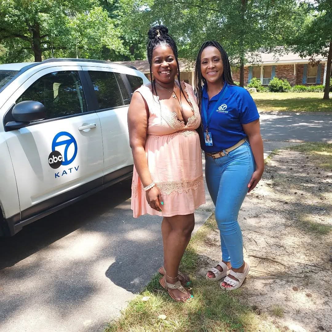 Two women standing outdoors near a white ABC 7 KATV news vehicle, smiling for the camera. One woman is wearing a pink dress, and the other is dressed in a blue polo shirt and light blue jeans.