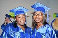 Two women wearing blue graduation caps and gowns smiling.
