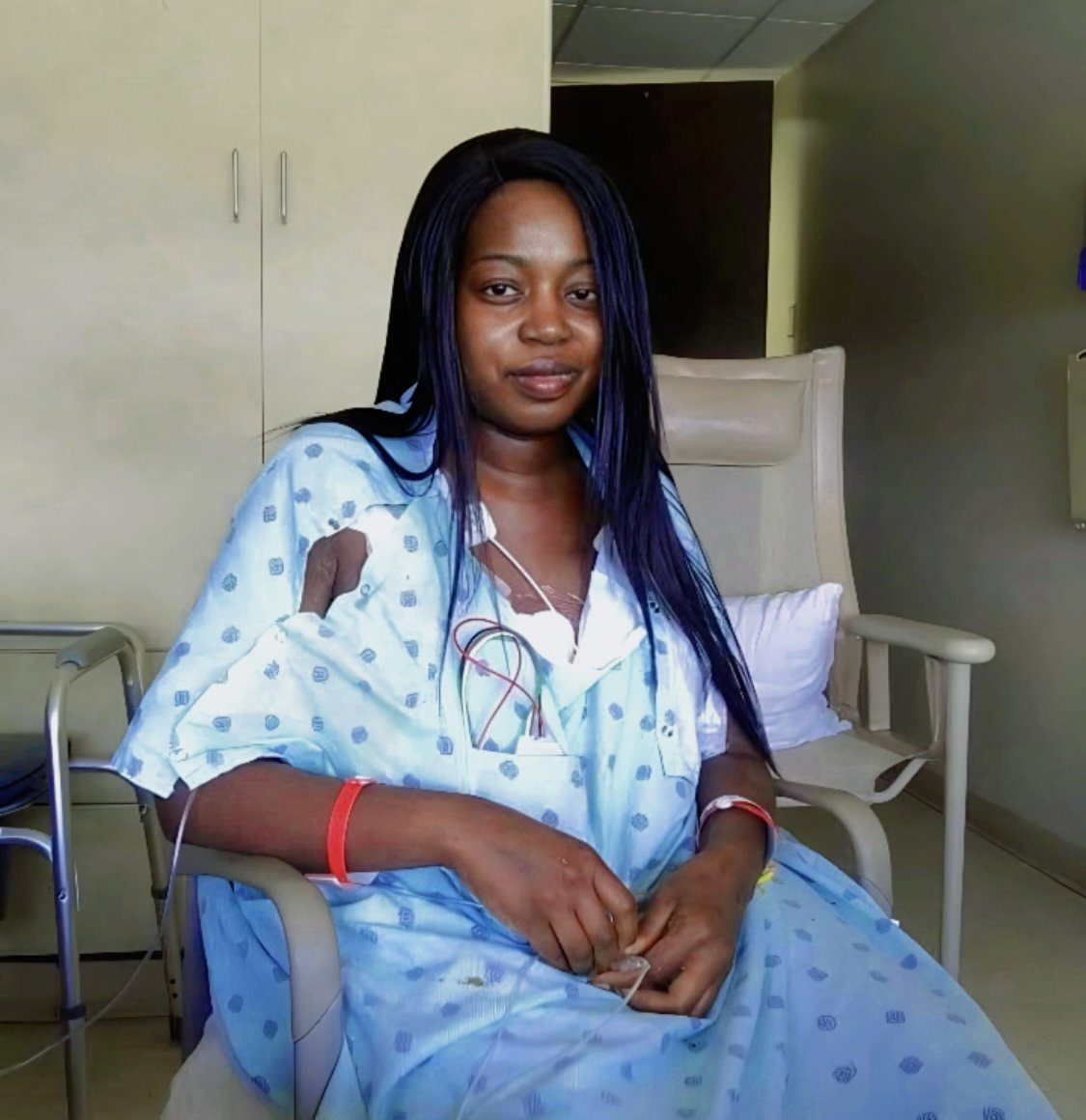 Woman in hospital bed with a smile, wearing hospital gown, in medical setting.